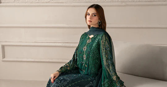 Woman wearing a green embroidered outfit sitting on a white couch against a beige wall.
