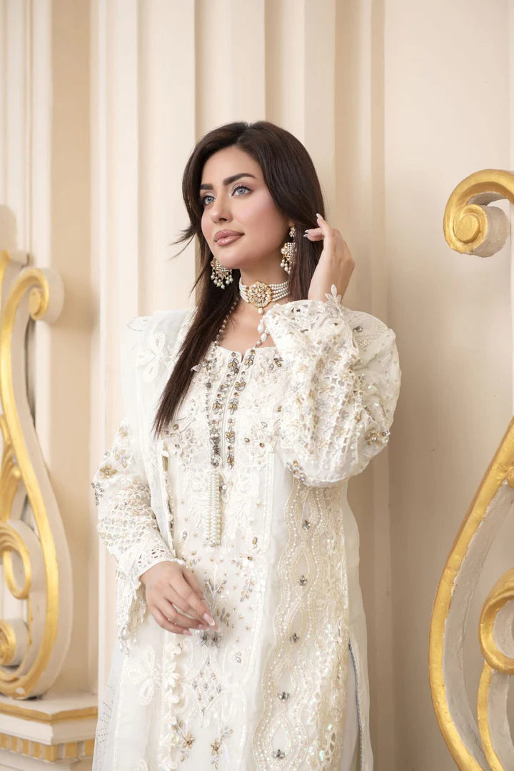 Woman in a white dress with intricate details against a decorative wall.