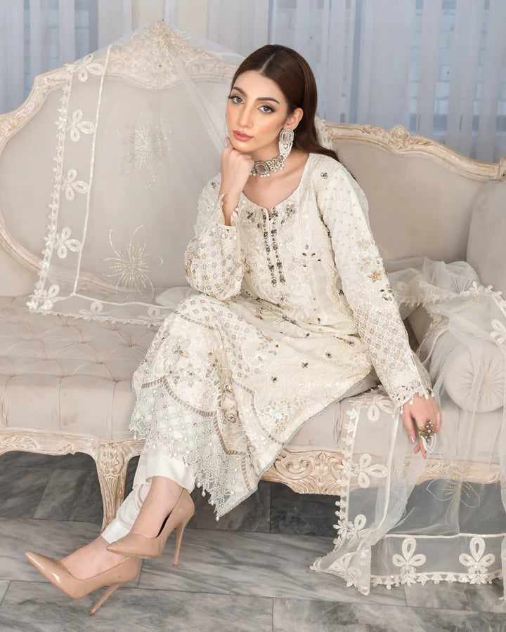 Woman in a white embroidered outfit sitting on an ornate sofa.