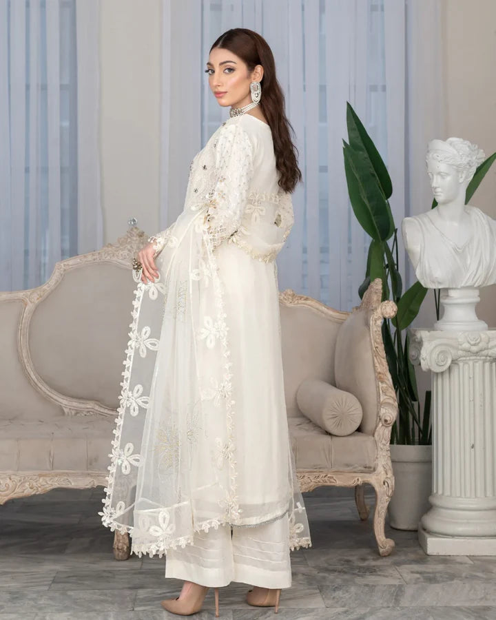 Woman in a white embroidered outfit standing in a stylish room with a sofa and decorative elements.